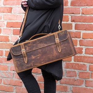 May include: A brown leather briefcase with a long strap and silver buckles. The bag is worn and has a distressed look.