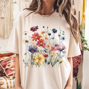 May include: A cream colored t-shirt with a watercolor floral print featuring pink, red, yellow, blue, and green flowers.