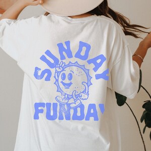 May include: White t-shirt with a blue graphic of a smiling sun with the text "SUNDAY FUNDAY" on the back.