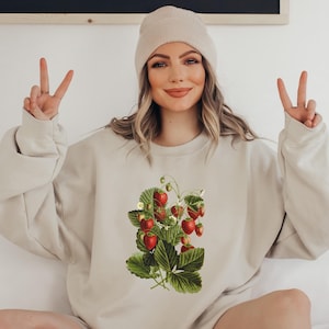 May include: A beige sweatshirt with a vintage illustration of a strawberry plant with red strawberries and green leaves.