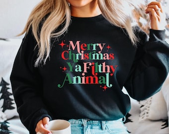 Puede incluir: Una sudadera negra con un estampado gráfico rojo, verde y rosa que dice "Feliz Navidad Ya Filthy Animal".