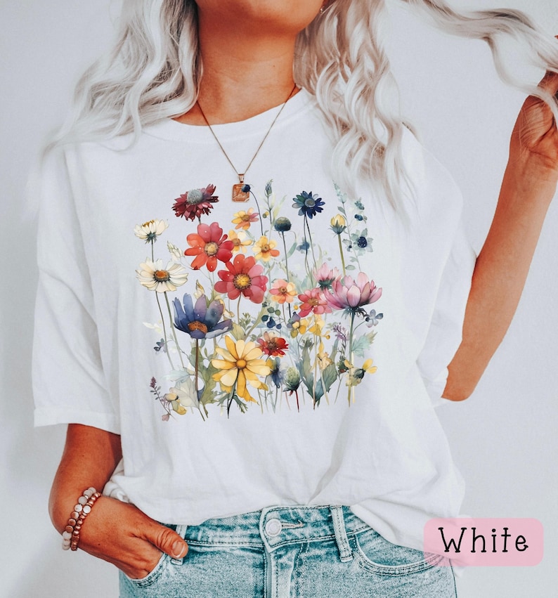 May include: White t-shirt with a watercolor floral print featuring a variety of colorful flowers and greenery.