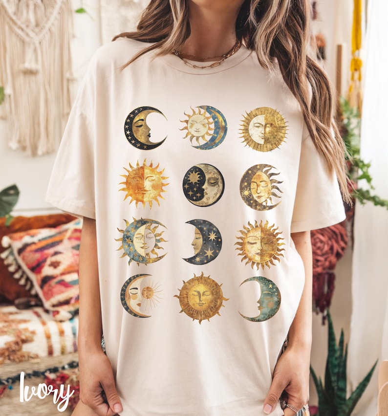May include: A cream-colored t-shirt with a graphic print of twelve different sun and moon phases in gold, blue, and black.