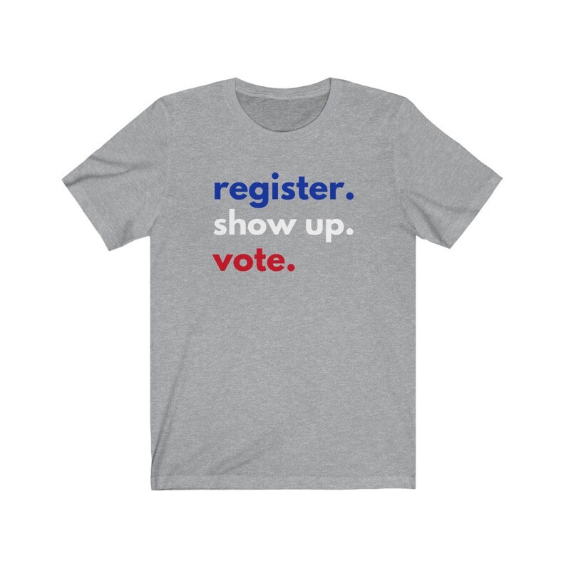 May include: A heather grey t-shirt with the text "register. show up. vote." in blue and red lettering.