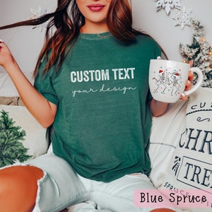 May include: A woman wearing a green t-shirt with the text "CUSTOM TEXT your design" on it. She is holding a white mug with a skeleton design on it. The mug has a red Santa hat on it.