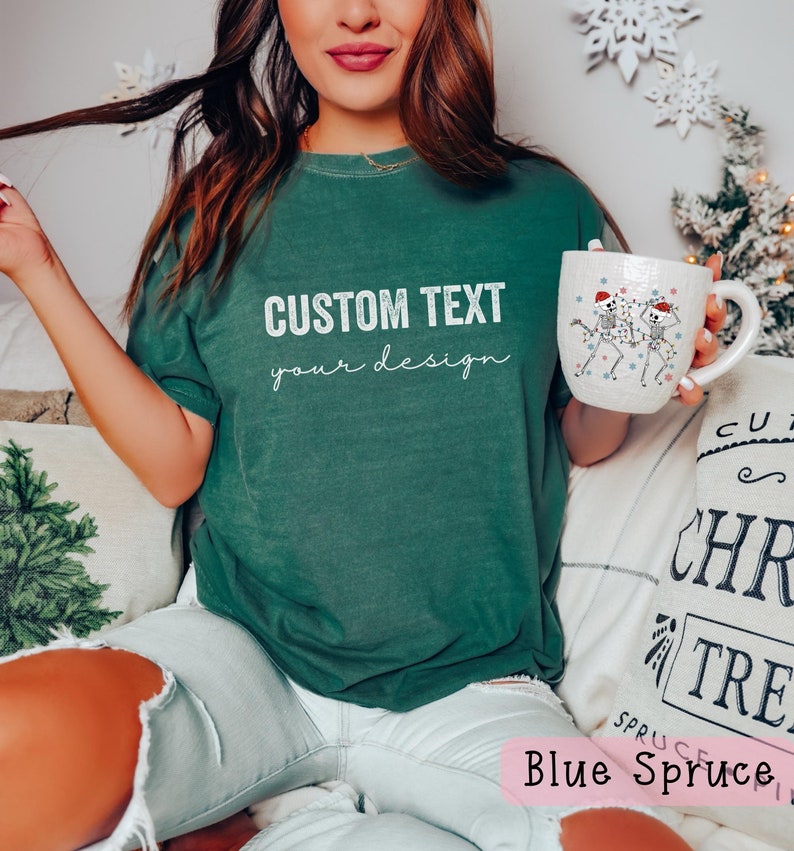 May include: A woman wearing a green t-shirt with the text "CUSTOM TEXT your design" on it. She is holding a white mug with a skeleton design on it. The mug has a red Santa hat on it.