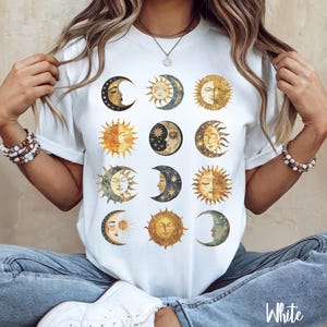 May include: White t-shirt with a graphic print of multiple suns and moons in gold, blue, and black.