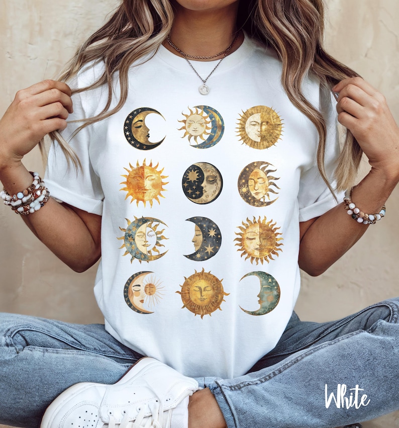 May include: White t-shirt with a graphic print of multiple suns and moons in gold, blue, and black.