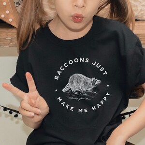 K&ouml;nnte beinhalten: Ein schwarzes T-Shirt mit einer wei&szlig;en Grafik eines Waschb&auml;ren und dem Text "Raccoons Just Make Me Happy".