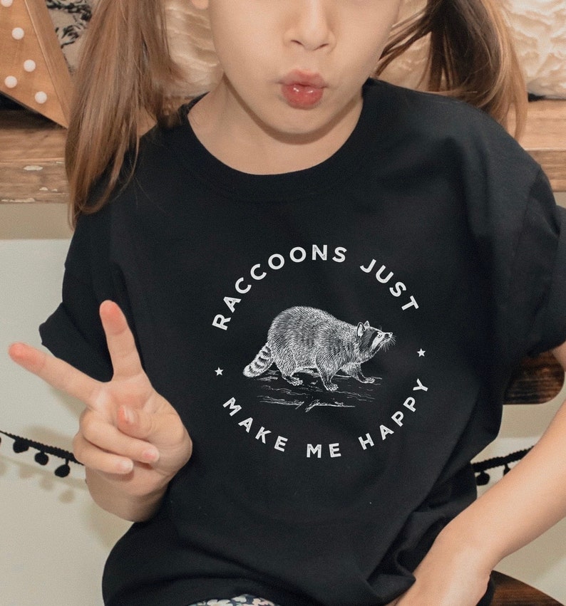 K&ouml;nnte beinhalten: Ein schwarzes T-Shirt mit einer wei&szlig;en Grafik eines Waschb&auml;ren und dem Text "Raccoons Just Make Me Happy".