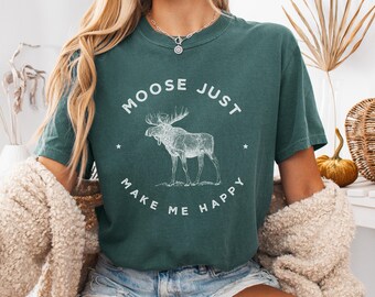 May include: A teal green t-shirt with the text "MOOSE JUST MAKE ME HAPPY" encircling a white illustration of a moose. The shirt is short-sleeved and made of a soft material.