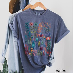 May include: A dark blue t-shirt with a floral print featuring colorful flowers and leaves. The shirt is made of a soft, comfortable material and has a relaxed fit.