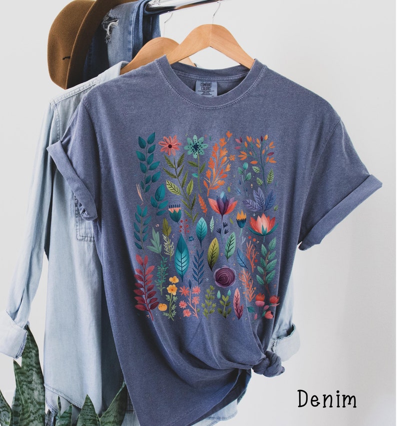 May include: A dark blue t-shirt with a floral print featuring colorful flowers and leaves. The shirt is made of a soft, comfortable material and has a relaxed fit.
