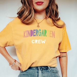 May include: A yellow t-shirt with the text "KINDERGARTEN CREW" in rainbow letters. The letters are in a rainbow gradient, with each letter a different color.