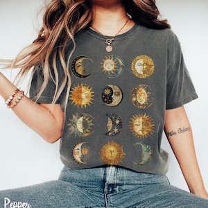 May include: A dark gray t-shirt with a vintage-style print of 12 moons and suns with faces. The print is in shades of gold, yellow, and blue.