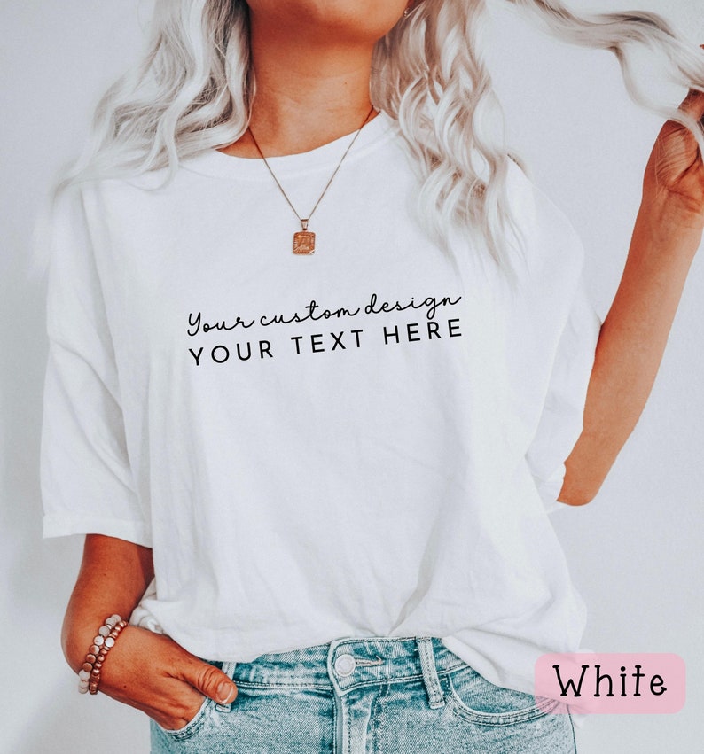 May include: White t-shirt with the text "Your custom design YOUR TEXT HERE" printed on the front. The shirt is being worn by a person with long blonde hair and is paired with blue jeans.