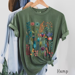 May include: A green t-shirt with a colorful floral print. The shirt is made of hemp.