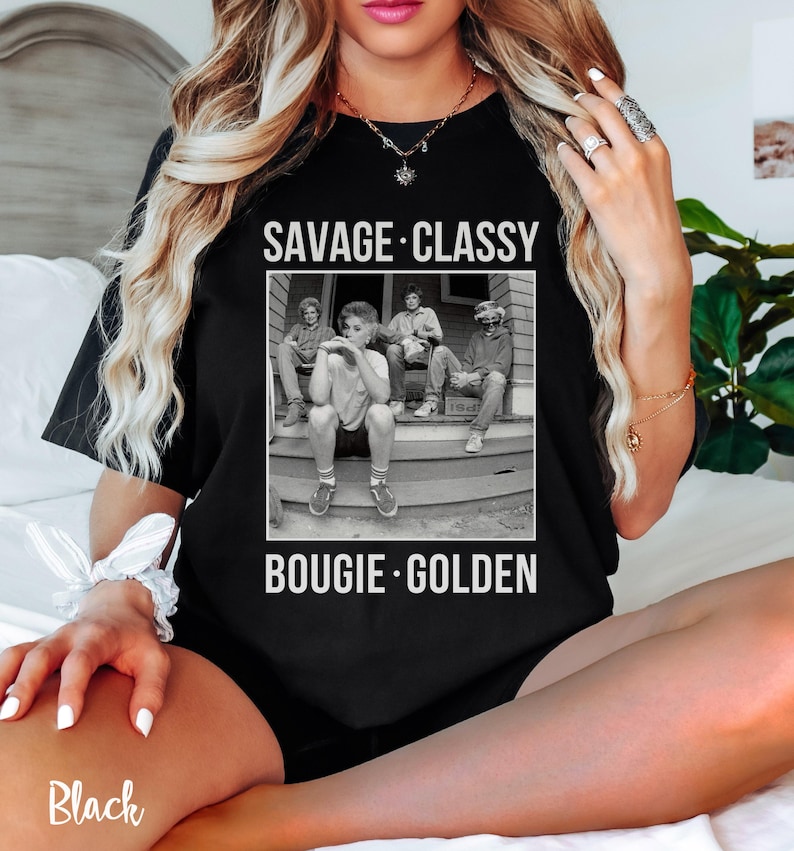 Puede incluir: Camiseta negra con un gr&aacute;fico de cuatro personas sentadas en un porche. El texto "Savage. Classy. Bougie. Golden." est&aacute; impreso en la camiseta.
