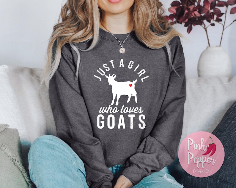 May include: A dark gray sweatshirt with the text "Just a girl who loves goats" in white lettering. A white silhouette of a goat with a red heart is in the center of the text.