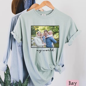 May include: A light green t-shirt with a framed photo of a family of four in a forest setting. The text "my world" is printed below the photo.