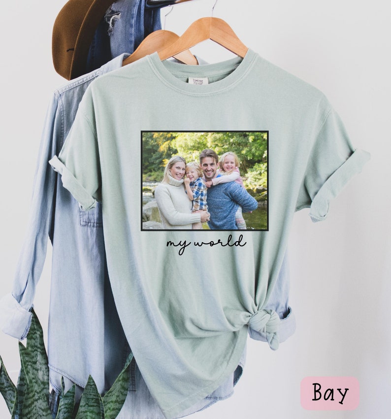 May include: A light green t-shirt with a framed photo of a family of four in a forest setting. The text "my world" is printed below the photo.