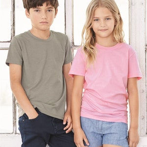 May include: Two children wearing t-shirts, a boy in a green t-shirt and blue jeans, and a girl in a pink t-shirt and blue denim shorts.