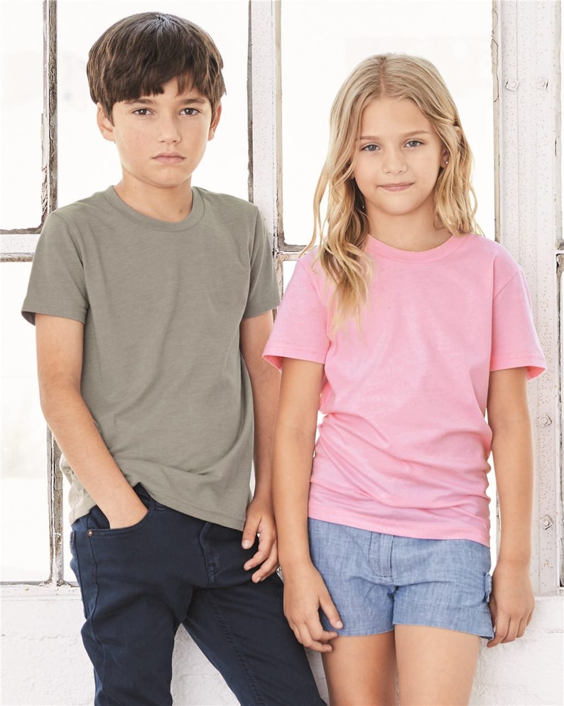 May include: Two children wearing t-shirts, a boy in a green t-shirt and blue jeans, and a girl in a pink t-shirt and blue denim shorts.