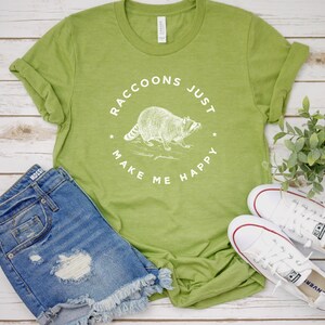K&ouml;nnte beinhalten: Ein gr&uuml;nes T-Shirt mit einer wei&szlig;en Grafik eines Waschb&auml;ren und dem Text "Raccoons Just Make Me Happy".