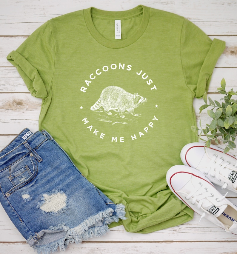K&ouml;nnte beinhalten: Ein gr&uuml;nes T-Shirt mit einer wei&szlig;en Grafik eines Waschb&auml;ren und dem Text "Raccoons Just Make Me Happy".