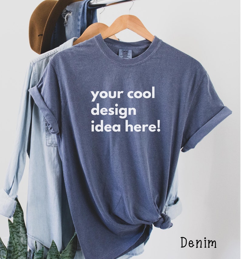 May include: A blue t-shirt with the text "your cool design idea here!" printed on the front. The shirt is hanging on a wooden hanger.