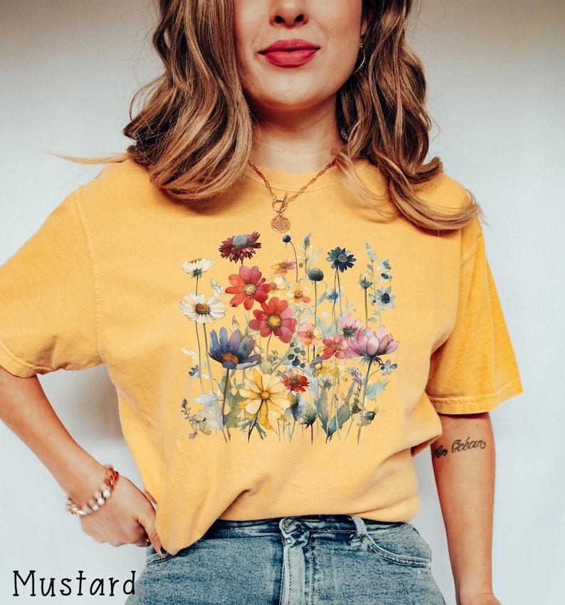May include: A mustard yellow t-shirt with a watercolor floral print. The flowers are in shades of pink, red, yellow, blue, and purple.
