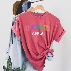May include: Red t-shirt with the text "Kindergarten Crew" in rainbow colors.