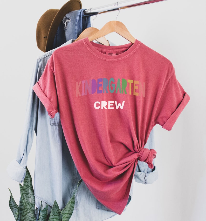 May include: Red t-shirt with the text "Kindergarten Crew" in rainbow colors.