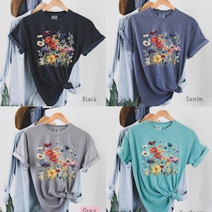 May include: A t-shirt with a floral print in shades of red, yellow, and blue. The shirt is available in four colors: black, denim, grey, and seafoam.