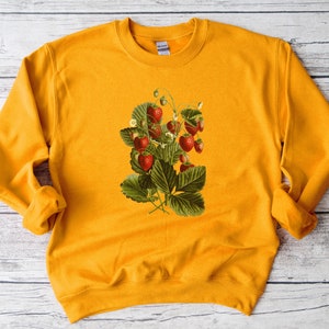 May include: A mustard yellow sweatshirt with a vintage illustration of a strawberry plant with red berries and green leaves.