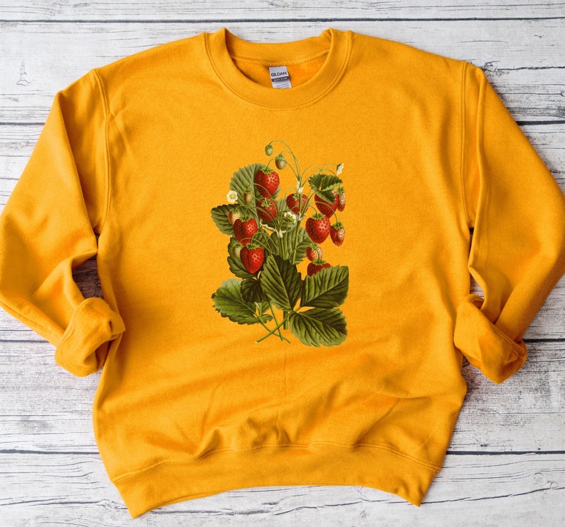 May include: A mustard yellow sweatshirt with a vintage illustration of a strawberry plant with red berries and green leaves.