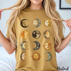 May include: A mustard yellow t-shirt with a repeating pattern of sun and moon faces. The sun and moon faces are in a vintage style with gold, blue, and white accents.