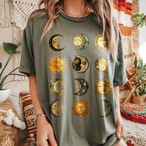 May include: A green t-shirt with a graphic print of multiple moons and suns in gold and blue.