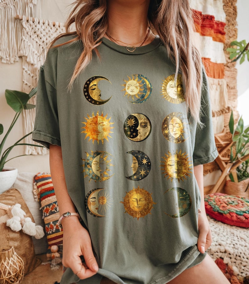 May include: A green t-shirt with a graphic print of multiple moons and suns in gold and blue.