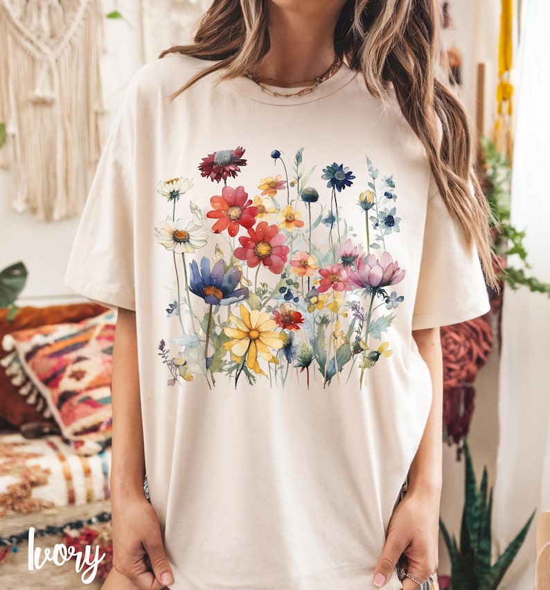 May include: A cream colored t-shirt with a watercolor floral print featuring pink, red, yellow, blue, and green flowers.