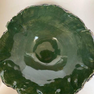 May include: A large, green ceramic bowl with a rough, textured rim. The bowl has a deep, rounded shape and a glossy finish.