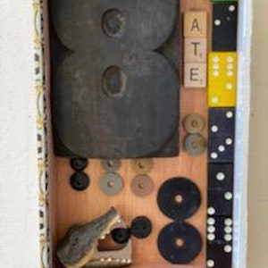 Puede incluir: Una caja de madera llena de varios artículos, incluyendo un gran número ocho de madera, una pequeña figura de cocodrilo, dados y fichas de letras que deletrean "ATE".