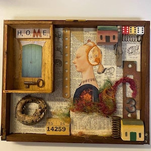 May include: A wooden box with a collage of various objects, including a portrait of a woman, a small wooden house, a key, a wooden ring, and a ruler with the numbers 14259. The box is filled with a newspaper print background.