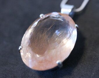 May include: A pink oval-shaped gemstone pendant with a silver chain. The gemstone has a clear, translucent appearance with a hint of brown.