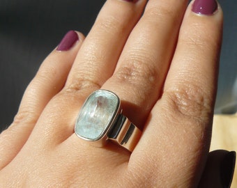 May include: A silver ring with a large, rectangular, light blue aquamarine gemstone. The ring is on a person's finger.