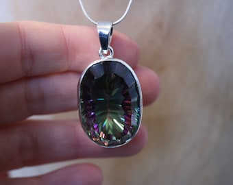 May include: A silver pendant with a large oval-shaped iridescent gemstone. The gemstone has shades of green, blue, purple, and black.