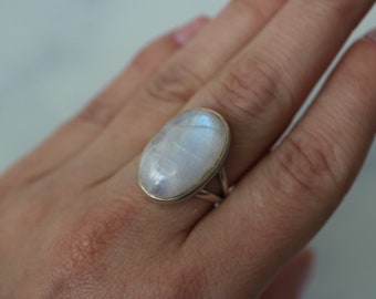 Puede incluir: Un anillo de plata con una gran piedra de luna ovalada. La piedra es blanca con un ligero brillo iridiscente.