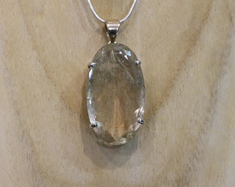 May include: A silver chain necklace with a large oval-shaped clear quartz pendant. The pendant has a faceted design and is set in a silver bezel.