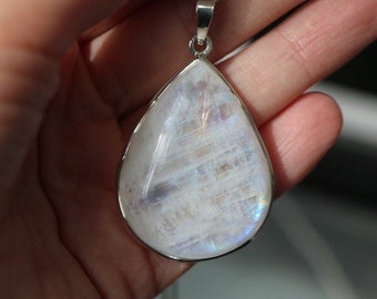May include: A teardrop-shaped pendant necklace with a white moonstone gemstone. The stone has a iridescent sheen and is set in a silver bezel.