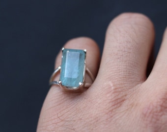 May include: A silver ring with a light blue rectangular gemstone. The ring is on a finger.